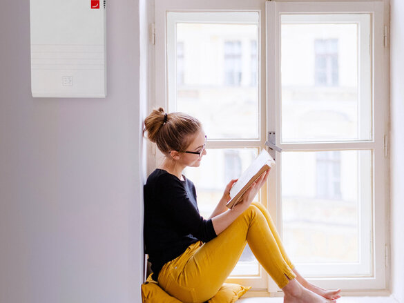 A young happy college female student with a book sitting on window sill at home, studying.