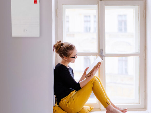 A young happy college female student with a book sitting on window sill at home, studying.