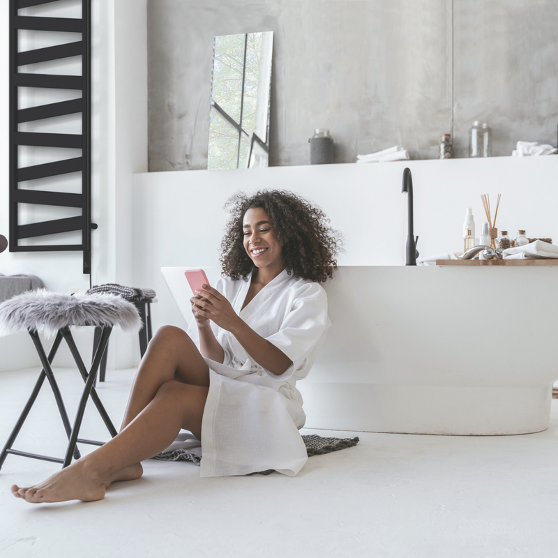 Smiling woman sitting in the bathroom on the floor with a smartphone in her hands