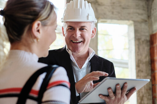 Sales agent talking with client in new building. Man working as realtor in construction site with customer. Real estate broker showing home to woman.