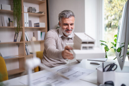Older architect, with house model, desk, office, working